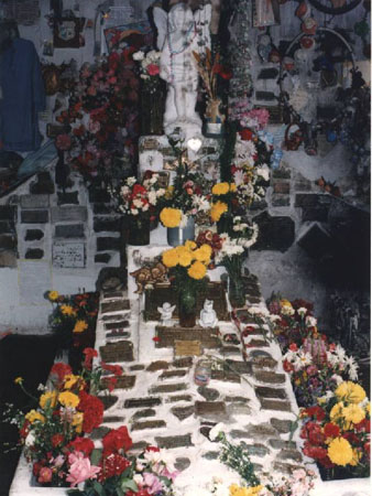 Tumba de Pedrito cubierta de unas 70 placas, en su mayor parte de bronce, y rodeada de flores y varios angelitos de porcelana